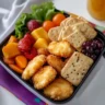 Chicken nugget Lunchable with cheese, crackers, fruit, and dipping sauce in a bento box.