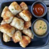 A plate of crispy homemade chicken nuggets with dipping sauces on a rustic wooden table.