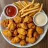 Plate of crispy Country Pride Chicken Nuggets with dipping sauces and fries.