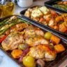 Three sheet pans filled with roasted salmon, chicken, tofu, and colorful vegetables like carrots, broccoli, and asparagus, styled on a ceramic table with natural lighting.