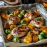 A sheet pan with perfectly roasted chicken breasts, Brussels sprouts, and butternut squash, styled as a simple, cozy dinner for two with minimal ingredients.