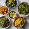 A vibrant top-down display of six Passover side dishes on a marble surface.