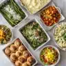 A colorful top-down spread of 10 catering side dishes on marble countertop