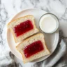 Top-down view of a jelly sandwich with milk on a wooden table.