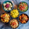 An overhead shot of various gluten free side dishes in colorful bowls on a marble surface.