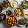 Shabbat side dish spread: cauliflower, salad, kugel, baba ghanoush, and more on marble.
