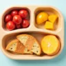 A colorful, divided toddler plate filled with easy lunch foods, including turkey roll-ups, sliced cucumbers, baby carrots, cheese cubes, apple slices, and whole grain crackers, with a sippy cup of water beside it on a wooden table.