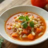 A bowl of steaming cabbage soup filled with chopped cabbage, carrots, celery, and tomatoes, served on a wooden table with a spoon beside it, promoting a healthy weight loss meal.