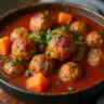 A close-up of a bowl filled with rich, dark brown Cajun meatball stew featuring large, tender meatballs simmered in thick gravy, garnished with chopped green onions, served alongside a scoop of white rice.