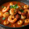 A hearty bowl of Cajun Ninja shrimp stew with plump shrimp, thick brown gravy, diced vegetables, and white rice served in the center, garnished with chopped green onions on top.