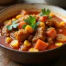 A hearty bowl of Caribbean stew featuring tender chunks of meat, vibrant vegetables like bell peppers and carrots, and rich, spicy broth, garnished with fresh herbs and served in a rustic ceramic bowl on a wooden table.