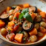 A bowl of hearty eggplant stew featuring tender chunks of eggplant, tomatoes, onions, and herbs, garnished with fresh parsley and served with a side of crusty bread on a rustic wooden table.