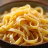 Freshly rolled and cut homemade noodles dusted with flour, resting on a wooden surface, ready to be cooked for chicken noodle soup.