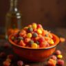 A variety of Halloween candy spread out on a table, including chocolate bars, lollipops, candy corn, and gummy treats, surrounded by festive decorations like plastic pumpkins, spider webs, and autumn leaves.